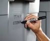 A hand is writing on a grey storage bin with a black Sharpie marker. Voir les images du produit