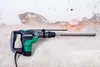 A power drill with a long drill bit attached, resting against a textured wall. Produktbild-Vorschau