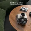 A pair of black headphones is placed on a wooden coffee table next to books and a decorative bowl. A green sofa is visible in the background. Produktbild-Vorschau