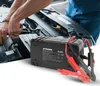 A person is working on a car engine, with a battery charger in the foreground. Náhled obrázku produktu