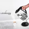 A hand is pouring hot water from a glass electric kettle into a white mug, with steam rising. Produktbild-Vorschau