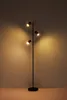 A black floor lamp with three adjustable spotlights is shown against a plain, textured wall. Podgląd zdjęcia produktu