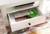 A close-up of a white drawer with items inside, placed on a rug. Produktbild-Vorschau