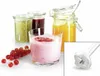 A close-up view of a glass of pink yogurt with berry topping, surrounded by jars of jam and a bunch of red currants, with an inset image of an immersion blender attachment. Náhľad obrázku produktu