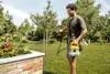 A man is using a Kärcher battery-powered pressure sprayer in a garden. Produktbild-Vorschau