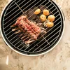 A rack of lamb and potatoes are grilling on a round charcoal grill. Produktbild-Vorschau