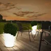 An outdoor patio scene at dusk with illuminated planters and chairs. Produktbild-Vorschau