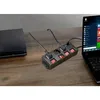 A power strip with multiple outlets and switches is connected to a laptop and a game console on a wooden desk. Produktbild-Vorschau