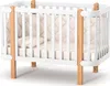 A white baby crib with natural wood accents, shown from a slightly elevated front-left angle against a white background. Produktbild-Vorschau