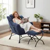 A woman is reading a magazine while sitting in a blue armchair with a matching ottoman in a living room. Produktbild-Vorschau