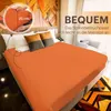 A bed with an orange fitted sheet and pillows, with a graphic design on the wall behind it. Produktbild-Vorschau
