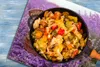 A close-up of a pan filled with cooked vegetables, placed on a surface that appears to be a printed image of a lavender field and a basket. Náhled obrázku produktu