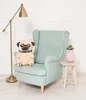 A plush pug dog sits on a light blue armchair next to a small white side table with a pink vase and a plant. A floor lamp is to the left. Voir les images du produit