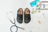 A pair of black Birkenstock clogs are laid out on a white surface with medical equipment. Anteprima dell’immagine prodotto