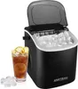 A black ice maker with its lid open, filled with ice cubes, next to a glass of iced tea with lemon slices. Several ice cubes are scattered in the foreground. Náhled obrázku produktu