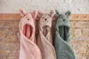 Three hooded blankets with animal faces hanging on hooks against a brick wall. Voir les images du produit