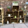 Wooden crates stacked and decorated with gardening items against a brick wall. Náhled obrázku produktu