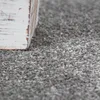 A close-up view of a textured gray carpet with the corner of a distressed white wooden object in the foreground. Produktbild-Vorschau
