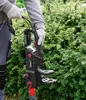 A person wearing gloves is holding an electric chainsaw in front of a green hedge. Produktbild-Vorschau