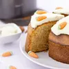 A close-up of a carrot cake with white frosting and decorative marzipan carrots. Produktbild-Vorschau