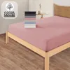 A pink fitted sheet is shown on a wooden bed frame, with a stack of folded sheets in various colors to the left. Produktbild-Vorschau