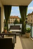 A balcony with outdoor furniture and curtains, overlooking buildings. Produktbild-Vorschau