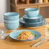 A set of blue and white striped ceramic dishes, including plates, bowls, and a serving bowl, are arranged on a wooden table. A plate of spaghetti is in the foreground. Náhled obrázku produktu