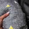 A hand is shown pressing into a soft, textured fabric with a geometric pattern of yellow and white triangles on a gray background. Another dark gray textured surface is visible in the background. Anteprima dell’immagine prodotto
