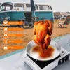 A roasted chicken on a rotisserie spit over a portable stove, with a vintage camper van and camping chairs in the background. Produktbild-Vorschau