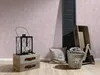 A decorative arrangement of home decor items including a lantern, wooden boxes, a basket with towels, and a cushion, set against a textured pink wall and wooden floor. Produktbild-Vorschau