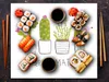 A flat lay image of sushi and chopsticks arranged around illustrated cacti and potted plants, with soy sauce dishes. Voir les images du produit