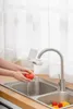 A person is washing a tomato under a modern kitchen faucet with an attached water filter device. Náhled obrázku produktu