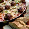 A close-up of a round stainless steel grill plate with meatballs and sauce, served with sliced bread. Podgląd zdjęcia produktu