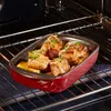A red baking dish with food inside is placed on an oven rack. Produktbild-Vorschau