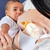 A baby is breastfeeding from a mother, with a breast milk collection bottle attached to the breast. Produktbild-Vorschau