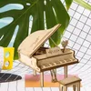 A wooden model of a grand piano with a small stool in front of it, set against a backdrop of a large green leaf and a grid pattern. Podgląd zdjęcia produktu