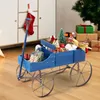 A blue wooden wagon filled with Christmas decorations and gifts, placed in a room with a Christmas tree and presents in the background. Produktbild-Vorschau