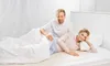 A couple is lying in bed, under a duvet, with the man resting his hand on the woman's hip. A heated underblanket is visible beneath them. Produktbild-Vorschau