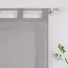 A close-up view of a grey fabric curtain with tab loops hanging from a metal curtain rod. A decorative antler-shaped finial is visible on the right end of the rod. A small branch with green leaves is in the lower right corner. Produktbild-Vorschau