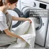 A woman is putting a white quilted blanket into a washing machine. Produktbild-Vorschau