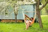Two women relaxing in a hammock in a garden with a small blue house in the background. Produktbild-Vorschau