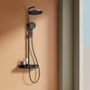 A black shower system with a round rain shower head and a handheld shower head is mounted on an orange wall. A small shelf holds two bottles of toiletries. Anteprima dell’immagine prodotto