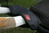 Close-up of a black stroller hand warmer with a red logo, attached to stroller handles covered in knitted sleeves. Produktbild-Vorschau