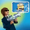 A boy in a suit and sunglasses holds a toy gun, aiming it at a Minion character displayed on a screen. Smoke emanates from the toy gun and the Minion. Náhled obrázku produktu