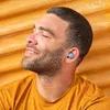 A man wearing blue earbuds and an orange t-shirt, with his eyes closed and a relaxed expression, against a textured orange and yellow background. Anteprima dell’immagine prodotto