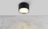 A black LED ceiling light fixture mounted on a white ceiling above a textured concrete wall. Podgląd zdjęcia produktu