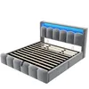 A grey upholstered bed frame with a slatted mattress base and blue LED lighting in the headboard, shown from a diagonal angle against a white background. Náhled obrázku produktu