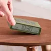 A hand is shown interacting with a digital alarm clock placed on a wooden table. Náhľad obrázku produktu