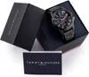 A Tommy Hilfiger watch is displayed in its open box, with the instruction manual placed in front. Produktbild-Vorschau
