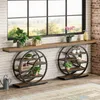 Two industrial-style console tables with circular shelving units are placed against a white brick wall, in front of a large window overlooking a landscape. Several potted plants are displayed on the tables and shelves. Anteprima dell’immagine prodotto